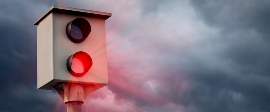 Ein rot auslösender Blitzer vor bewölktem Himmel.