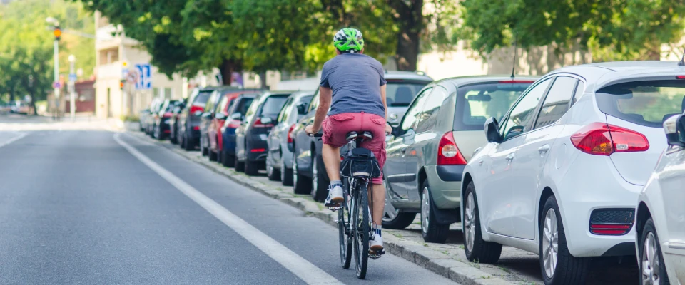 Radfahrer fährt an parkenden Autos vorbei