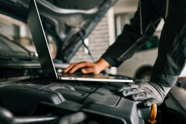 Ein Kfz-Mechaniker mit einem Laptop an einem Automotor