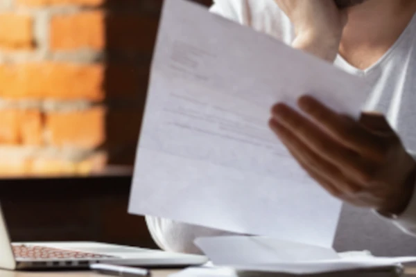 Ein Mann sitzt am Laptop mit einem Bußgeldbescheid in der Hand