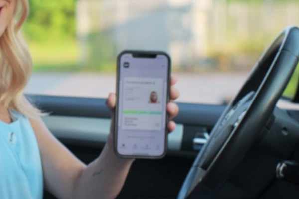 Frau im Auto mit digitalem Führerschein auf dem Handy