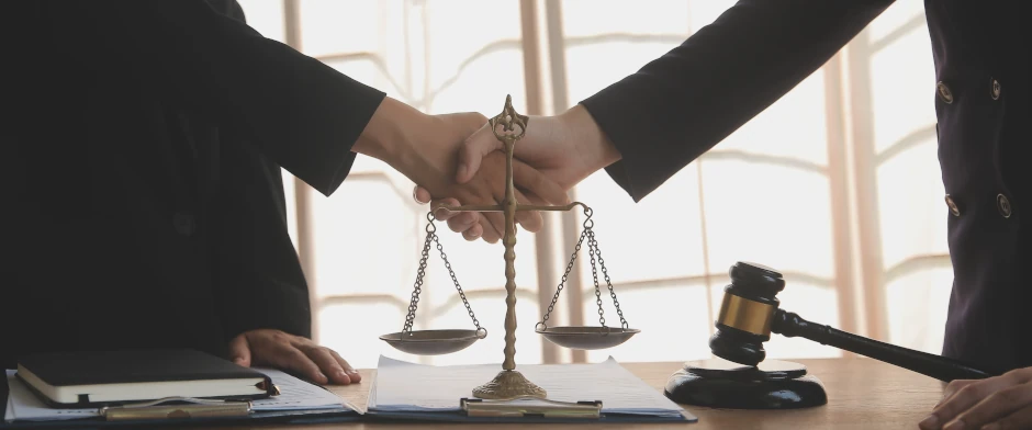Zwei Personen reichen sich über einer Justitia-Waage die Hand 